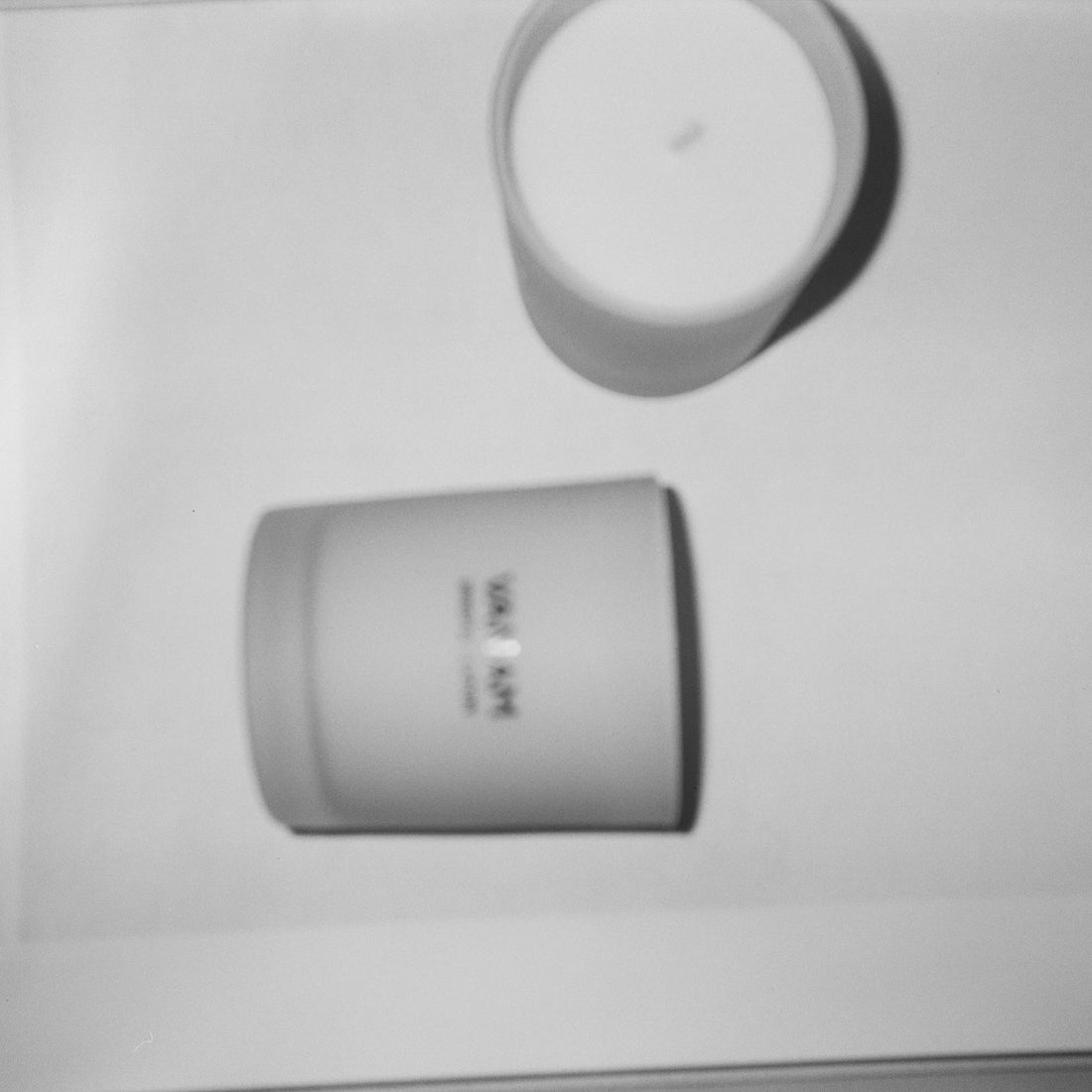 Two Vanam Studios scented candles in matte white vessels     │ │ Candles Worth It? │ photographed from above in black and white